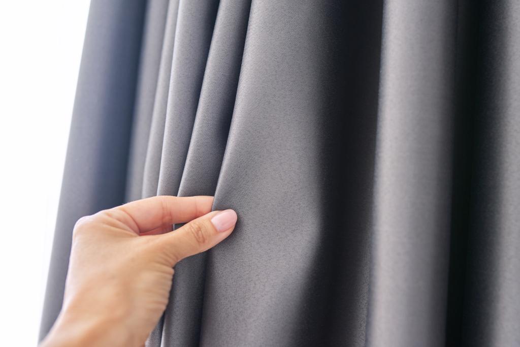 Woman's hand touching curtain, gray blackout fabric, light-blocking fabric